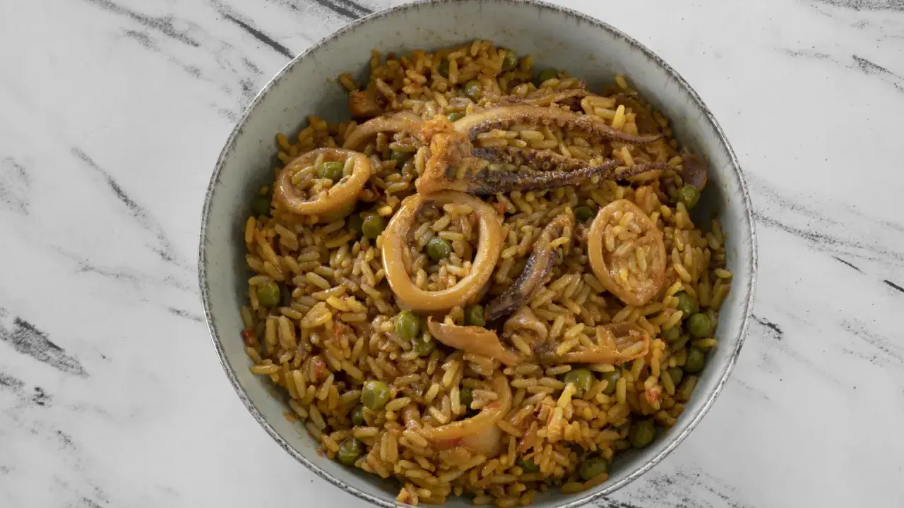 Un delicioso plato de arroz con calamares y guisantes, servido en un cuenco sobre una superficie de mármol.