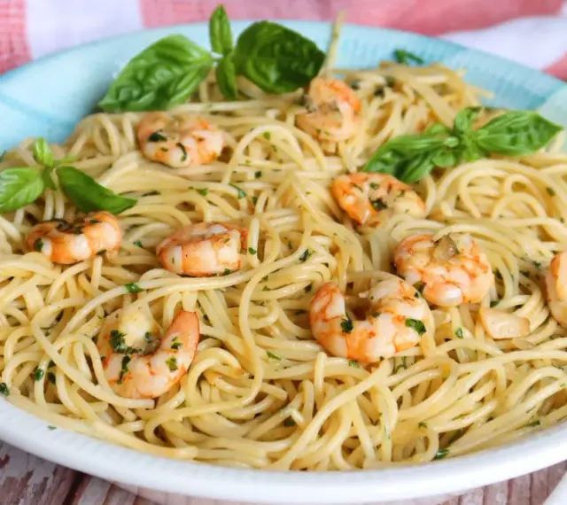 Un plato de espaguetis con gambas, adornado con hojas de albahaca fresca y perejil picado.