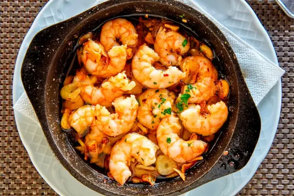 Un plato humeante de langostinos al ajillo, jugosos y dorados, nadando en aceite de oliva con ajo y perejil. ¡Un manjar irresistible!
