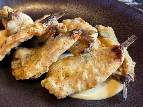 Crujientes boquerones fritos, dorados y servidos sobre una cremosa salsa.