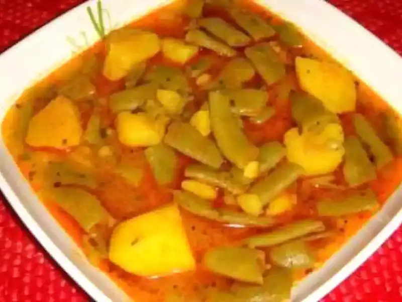 Un plato humeante de judías verdes con patatas, cocinado en una sabrosa salsa rojiza.