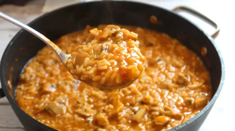 Cuchara llena de cremoso arroz con pollo de la abuela, humeante y con trozos de pollo y champiñones.