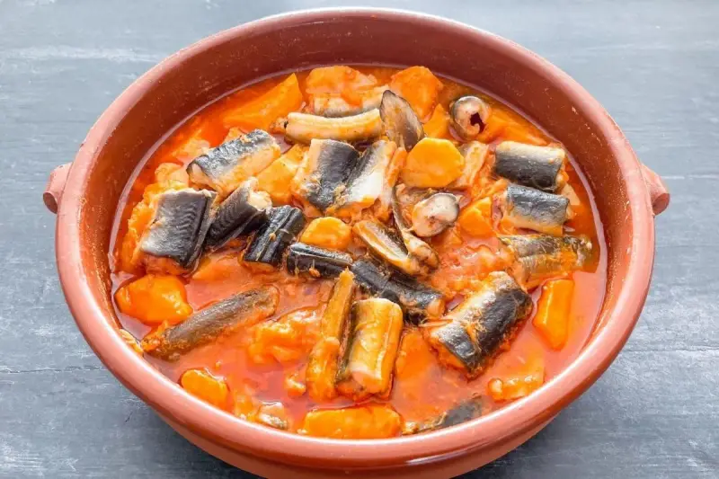 Un cuenco de barro con un sabroso all i pebre, un guiso tradicional de anguila y patatas en salsa roja.