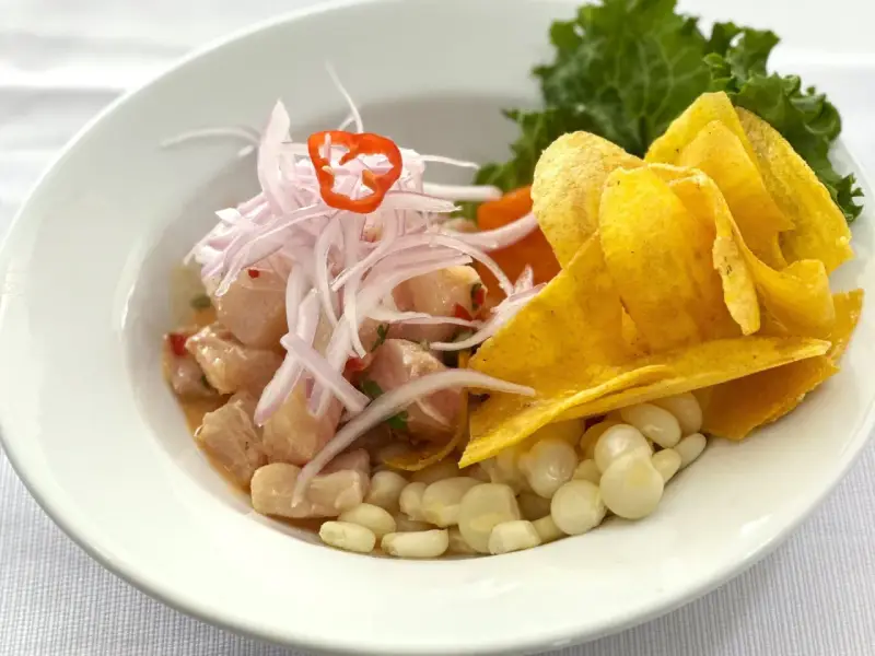 Delicioso ceviche peruano con trozos de pescado fresco, cebolla morada, chile, maíz tierno y chips de plátano.